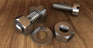 A group of bolts and nuts with flat washers on a wood surface.
